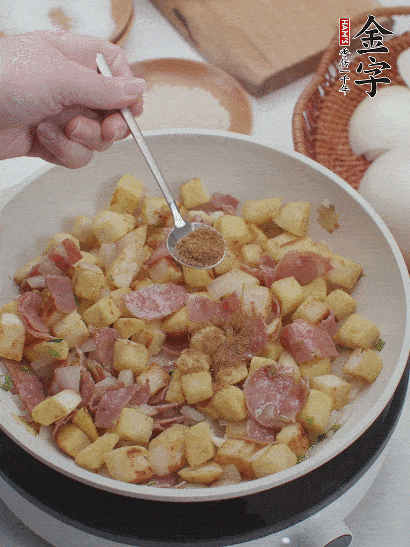 起鍋少油，煸香洋蔥丁、蔥白，加入金字培根火腿翻炒幾下，再加入饅頭丁、1小勺孜然粉、少許鹽翻炒均勻并鋪平。