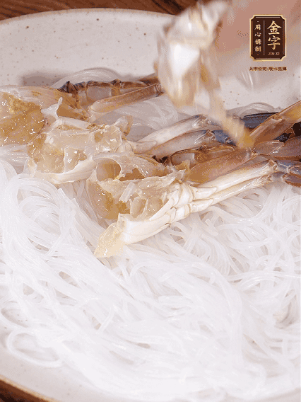 盤底墊上粉絲，擺上梭子蟹、火腿片，撒姜粒，淋上蒸魚豉油、花雕酒調(diào)味腌制15分鐘